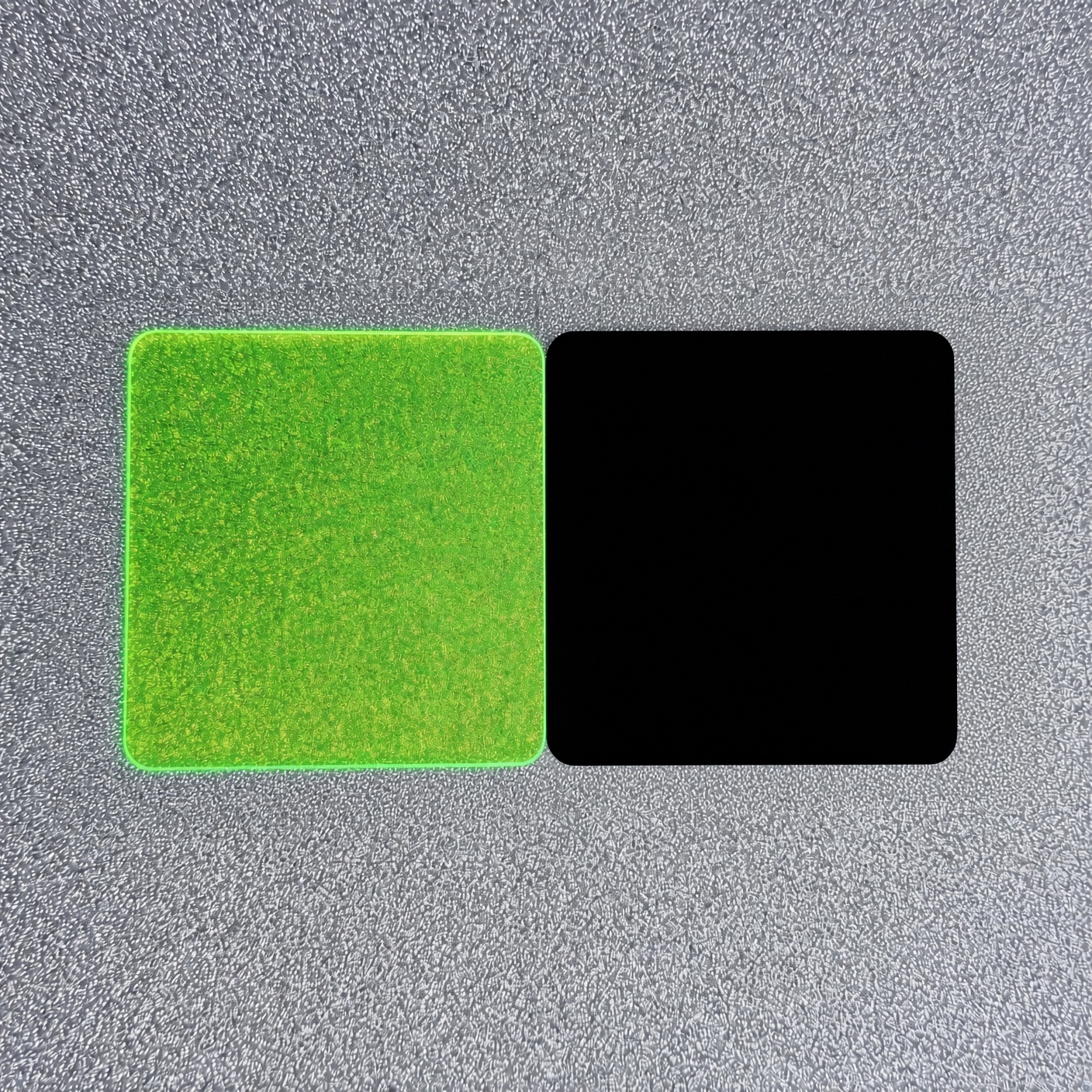 Zwei Zuschnitte aus PLEXIGLAS® auf grauem Untergrund: links Neongrün mit leuchtender Kante, rechts Schwarz