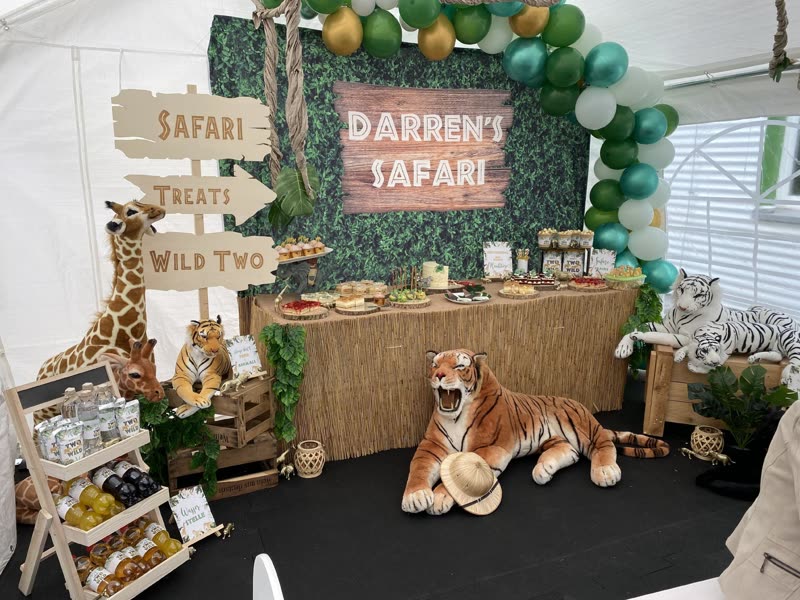 Safari-Partydeko im Zelt mit Holzschild „Darren’s Safari“, Wegweiser und Plüschtieren