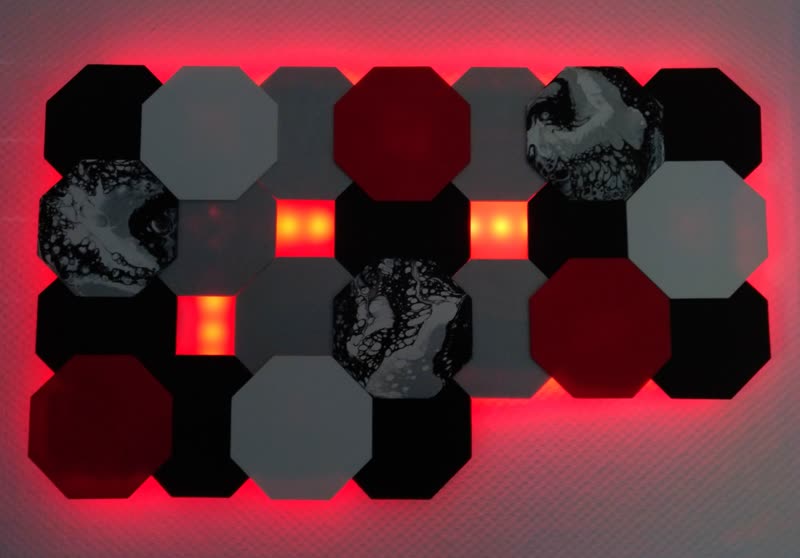 Wandlampe aus achteckigen Holzplatten im abgedunkelten Raum, rot hinterleuchtet