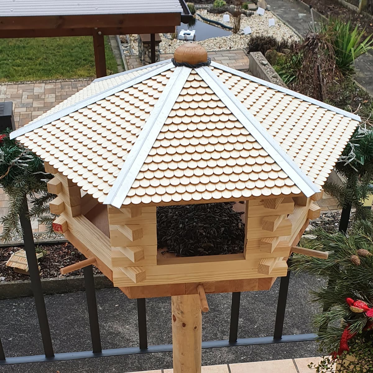 Vogelhaus mit gedecktem Schindeldach aus vielen runden Holzschindeln, gefüllt mit Sonnenblumenkernen
